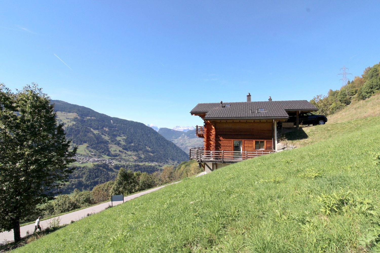 Chalet voisin en madrier avec balcon, le pré au premier plan et la vallée qui descend vers Le Châble.